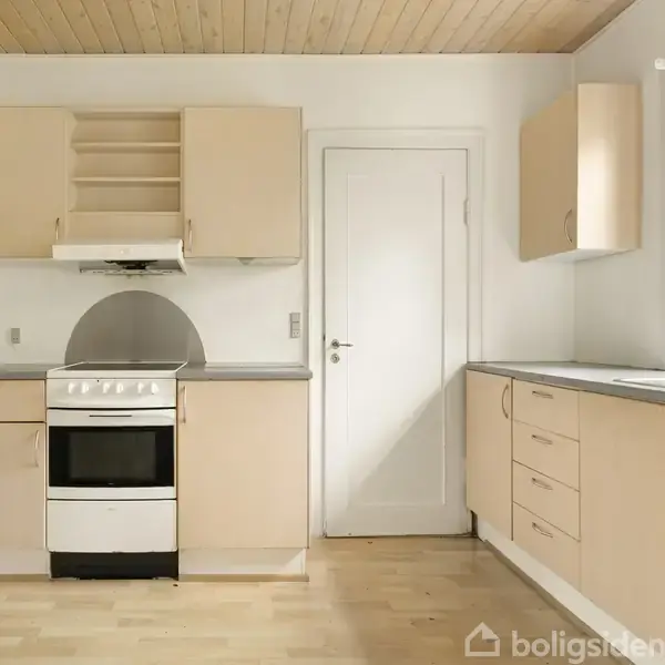 Et lyst køkken med hvid komfur og træskabe står ved en væg. Skabene mangler døre. Et stort vindue og en rød lampe er synlige. Trægulv og panelloft dominerer.