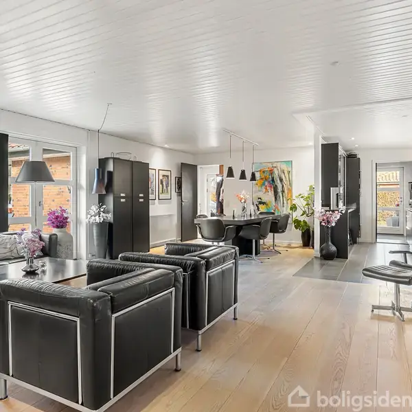 Stue med sorte lædermøbler, spisestue og kunstmaleri. Store vinduer slipper lys ind, og lyse trægulve strækker sig gennem rummet. Moderne indretning med minimalistisk dekoration i boligmiljø.