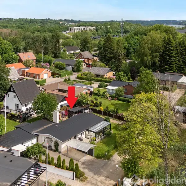 Rødt taghus markeres med en rød pil i et grønt boligområde med mange træer og flere omkringliggende huse.