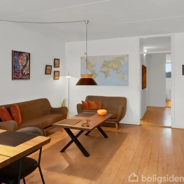 En stue med to brune sofaer står omkring et bord med en orange skål. Væggene er dekoreret med billeder og et verdenskort. Plankegulv og indbydende belysning.