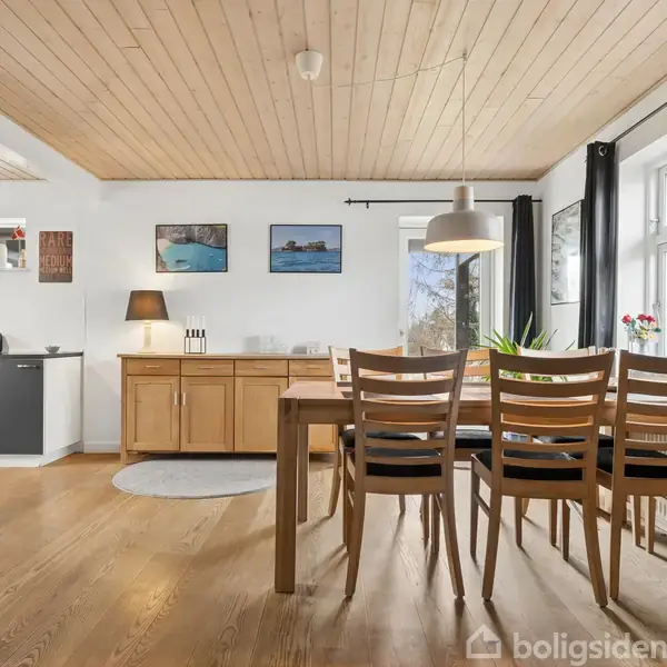 Brun lædersofa med puder står i hjørnet af en skandinavisk stue. En moderne lysekrone hænger over et sofabord. Plante i hjørnet og store vinduer lyser rummet op.
