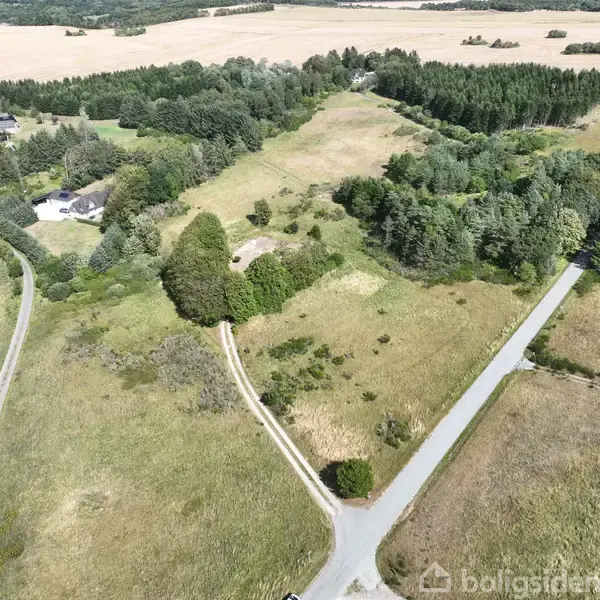 Luftfoto af landskab med marker og to veje, der krydser i et T-kryds. Området er omgivet af skovbevoksning og enkelte bygninger.
