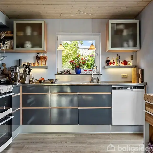 Moderne køkken med mørke, skinnende skabe; peberkværn, blender og flere apparater står på bordpladen. Et vindue med planter over vasken og opvaskemaskine ved siden af. Træloft og gulv.