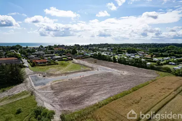 En byggeplads under opførelse med jordarbejde i en forstadsmæssig omgivelser nær kysten, omgivet af huse og grønne områder.