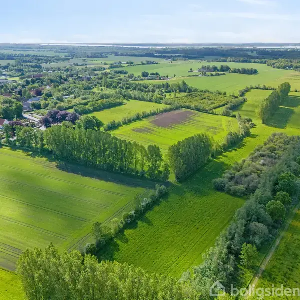 Grønt landskab strækker sig over marker og klippekanter, med en landsby i baggrunden under en klar himmel.