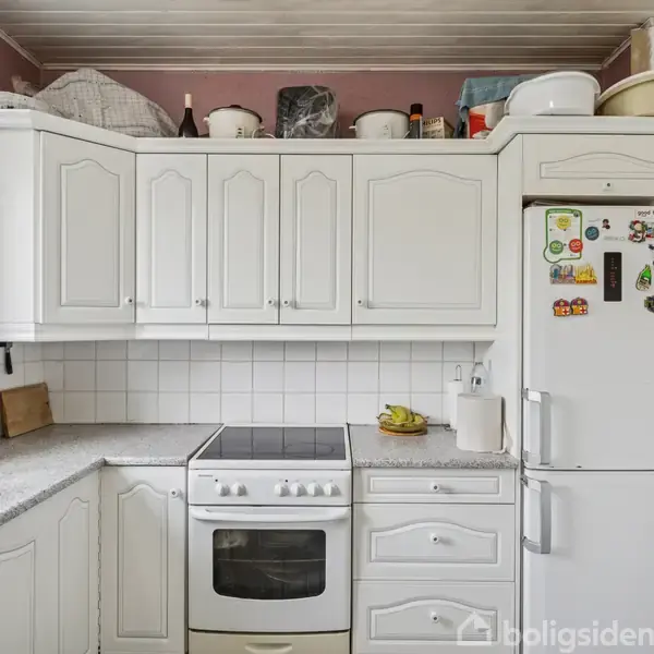 Et hvidt køkken med overskabe og skuffer omringer en ovn med keramisk kogeplade. Køleskabet har magneter og står ved siden af en vask i et lille, lyst rum.