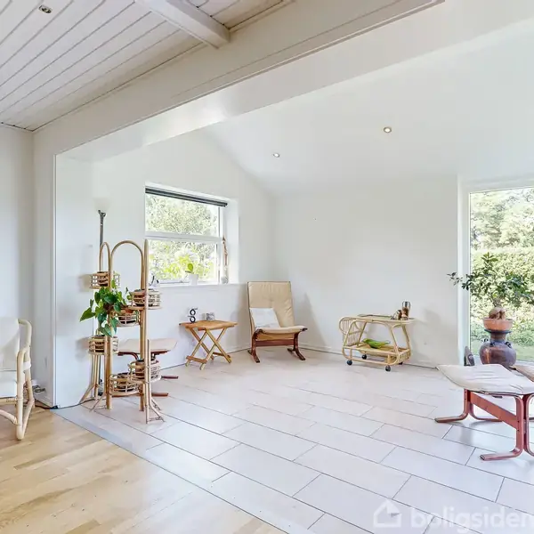 Stue med lyse trægulve og hvidmalede vægge. To elegante liggestole står foran store vinduer, der vender ud mod en grøn have. Indretningen er minimalistisk med bløde nuancer.
