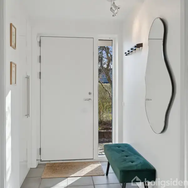 Dør står åben og fører ud til en have. Indendørs er der en skæv spejl på væggen og en blå bænk. Krogen er monteret over bænken.