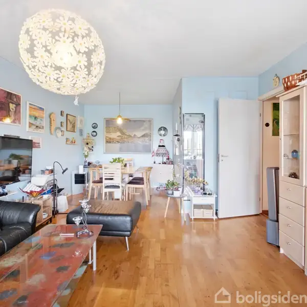 Moderne stue med sort lædersofa, sofabord, billeder og kunst på lyseblå vægge; spisebord i baggrunden; stor, blomsterformet loftslampe; trægulv, reoler, skabe og dekorationer.