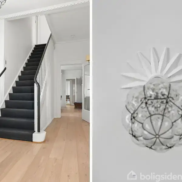 Lang spisebord omgivet af polstrede stole står i en lys spisestue med store vinduer, der viser en grøn have. Moderne lysekrone hænger over bordet, kufferter står i hjørnet.