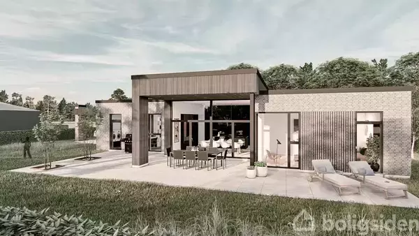 Moderne hus med store vinduer og fladt tag, omgivet af en terrasse med spisebord og liggestole. Græsplæne og træer skaber en rolig haveatmosfære.