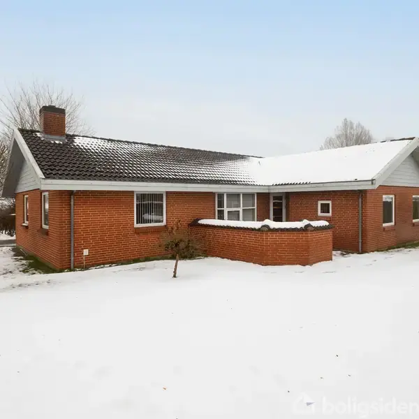 En rød murstensvilla står stille i et snedækket landskab med nøgne træer. Huset har et mørkt tag og et udendørs skorstensrør.