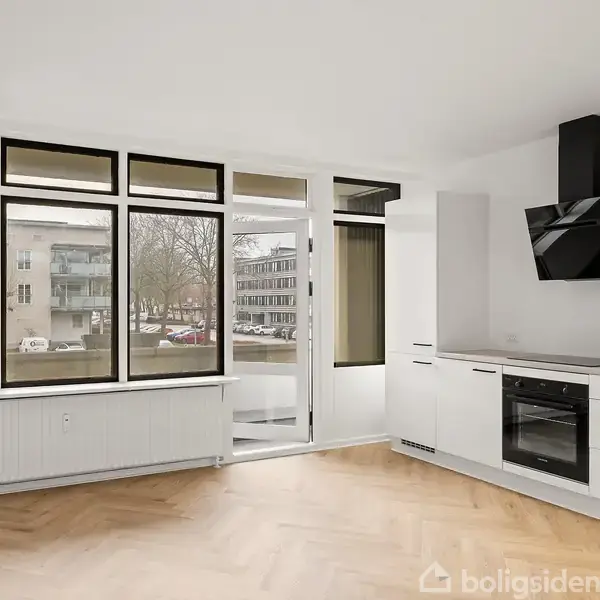 Lyst køkken i moderne design med sorte og hvide skabe. Store vinduer giver udsigt til en beboelsesgade med træer og biler. Trægulve i sildebensmønster fuldender rummet.