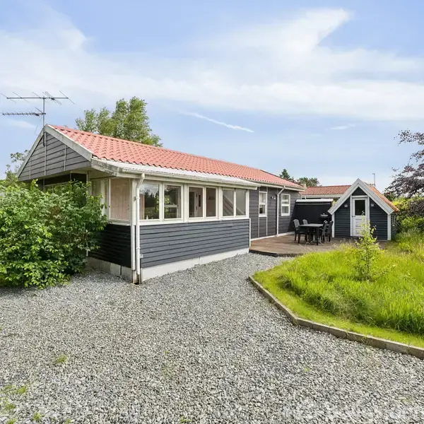 Et sort-hvidt hus med nummeret 90 på siden står stille. Det har et rødt tegltag, omgivet af en grusvej og grønne marker.