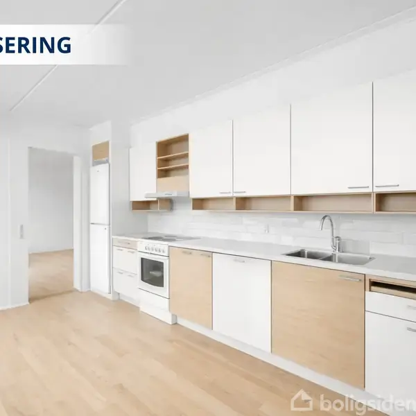 Køkken med lyse trægulve, hvide og lysebrune skabe og skuffer. Indbygget komfur, ovn og opvaskemaskine under hvide skabe. Vask integreret i bordpladen. Tekst: "VISUALISERING".