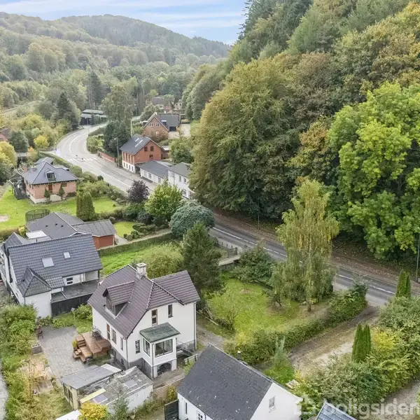 Huse med mørke tage ligger langs en snoet vej i en frodig dal ved siden af en flod. Omkringliggende områder er præget af tætte skove og skovklædte bakker.
