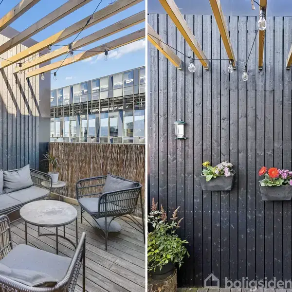 Terrassesæt består af grå sofa og stole omkring et lille, rundt bord; omgivet af en sort trævæg med blomsterkrukker. Trævæggen har lameller og lyskæder, bymiljø ses i baggrunden.