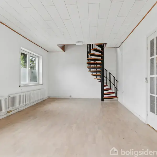 Køkkenskabe i træ står fast monteret. Der er hylder og skuffer. Rummet har en åbning til en tilstødende gang. Gulvet er lyst træ, og væggene har flisemønster.