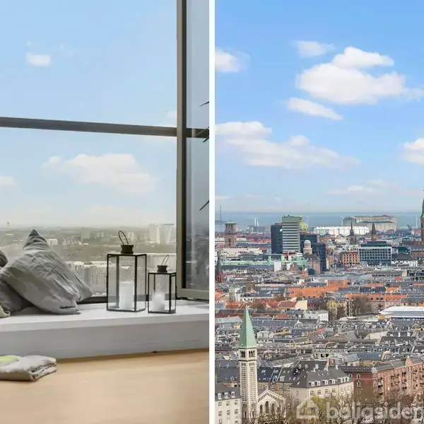 Vindu med siddeplads fyldt med puder og lanterner, kigger ud over byens skyline med mange bygninger og nogle kirketårne under en blå himmel med skyer.