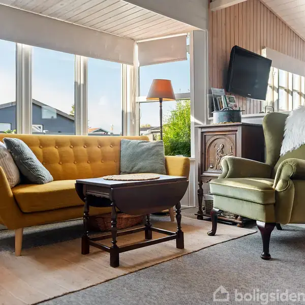 En gul sofa og en grøn lænestol står ved siden af hinanden omkring et lille bord i en lys stue med store vinduer. En lampe og en vægmonteret tv-skærm ses bagved.