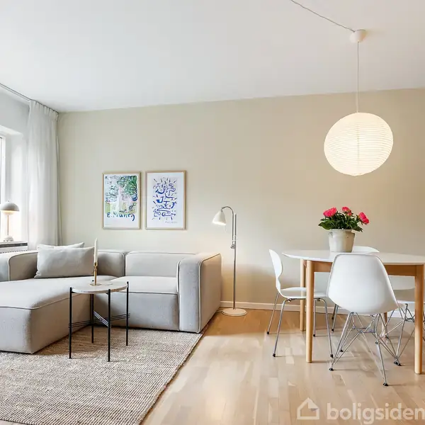 En lys stue med en grå hjørnesofa. Et sofabord står ved siden af sofaen. Ved spisebordet med hvide stole hænger en lampe. En guitar står i hjørnet.