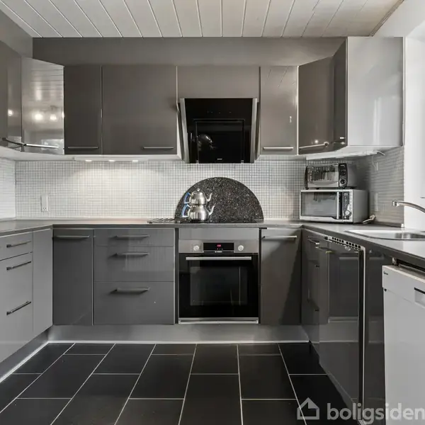 Et moderne køkken med grå skabe, hvor en indbygget ovn og mikroovn står midt i. En orkidé i vindueskarmen tilføjer farve, mens et lyst flisebelagt backsplash lyser op.