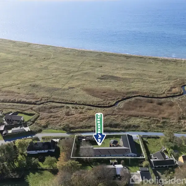 Hus markeret med en pil står blandt flere boliger; baggrund er en strand med åbent hav og græsarealer. Tekst: "90 Solgt".