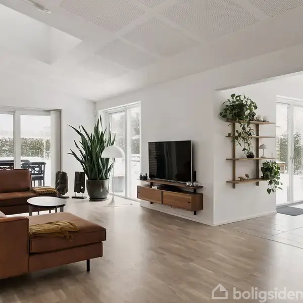 Brun sofa står i en lys stue, med et fladskærms-tv på en vægmonteret hylde. Store planter og et spisebord ses nær glasskydedøre, der åbner ud til en terrasse.