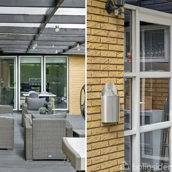 Rattanmøbler står på en overdækket terrasse med en glasoverdækning, flankeret af gule murstensvægge. Store glasdøre fører ind til huset, og en havelampe er monteret på væggen.