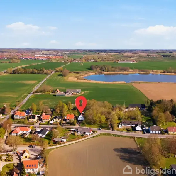 Rødt kortikon markerer et hus i en landsby omgivet af marker og en sø i baggrunden. Området er grønt og fredeligt med spredte huse og skovområder.