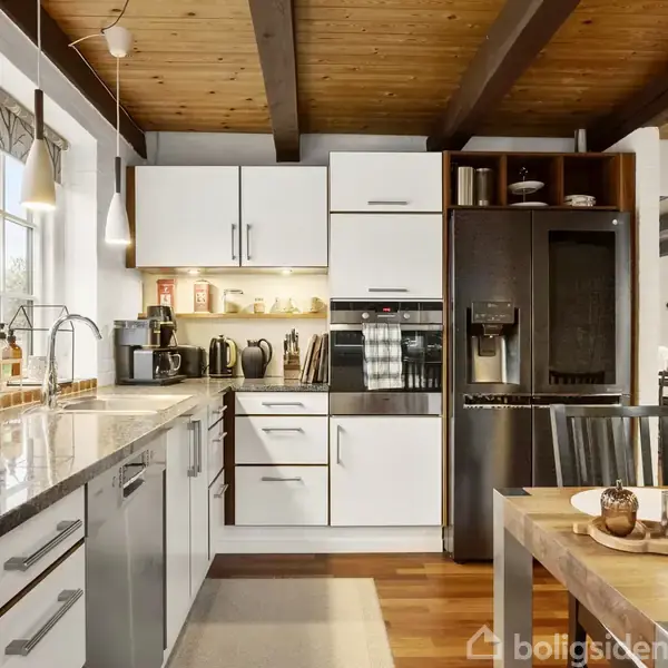 Køkken med hvide skabe, kaffemaskiner og indbygget ovn står under en træbjælket loft. Et spisebord med dækkede tallerkener er i forgrunden, mens vinduer langs væggen giver naturligt lys.