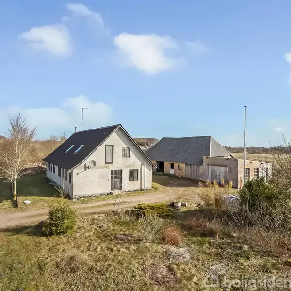 To bygninger står side om side på en åben mark med en vej til venstre. Skyer og blå himmel i baggrunden.