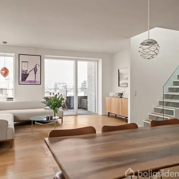 Stue med en stor træbord i forgrunden, sofa mod en glasdør der leder til altan. Stairs med glasrækværk til højre; ovenlys illustrerer moderne design.