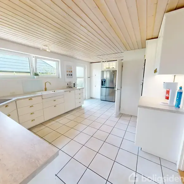 Stue med to mørkerøde sofaer og et sofabord. En pejs og en fladskærm hænger på stenvæggen. Store vinduer giver lys ind, og to bordlamper står tændte.