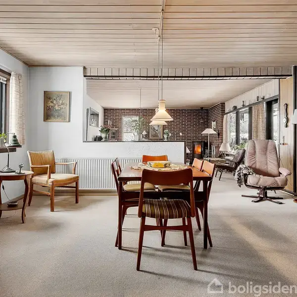 Et åbent rum med vintage møbler, herunder spisebord og stole. Der er store vinduer, der slipper lys ind, og vægdekorationer i et hyggeligt og klassisk hjem.