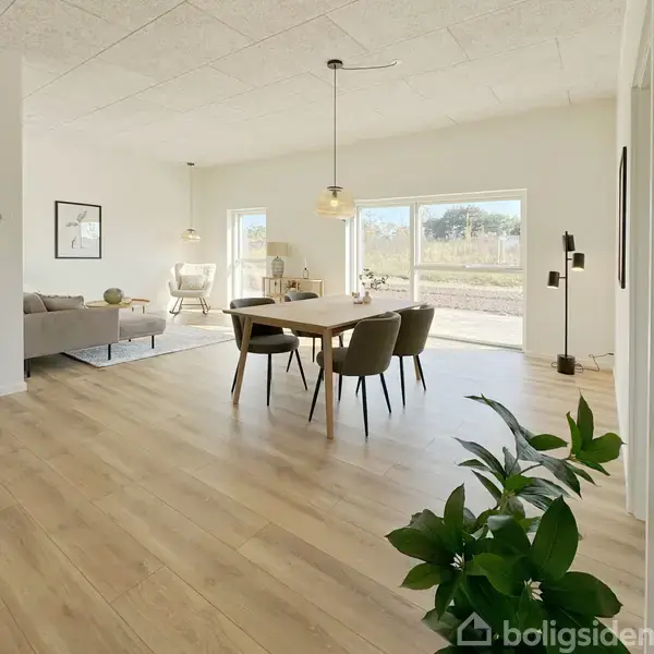 Spisebord omgivet af stole står på trægulv i lys stue med store vinduer. Sofa og lænestol i baggrunden, med minimalistisk dekoration og indendørs planter. Opkvikkende dagslys fylder rummet.