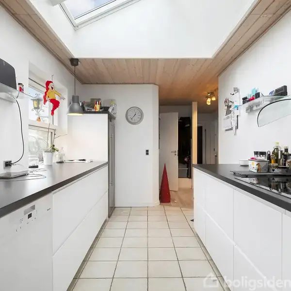 Et moderne køkken med hvide skabe og sorte bordplader. Knive hænger på en væg. Et stort vindue slipper lys ind, og der er redskaber og udsmykninger langs væggene.