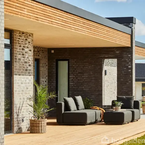 Hus med moderne design har en terrasse med komfortable sofamøbler og planter. Sollys oplyser scenen, mens grønne områder og andre huse ses i baggrunden under en blå himmel med skyer.