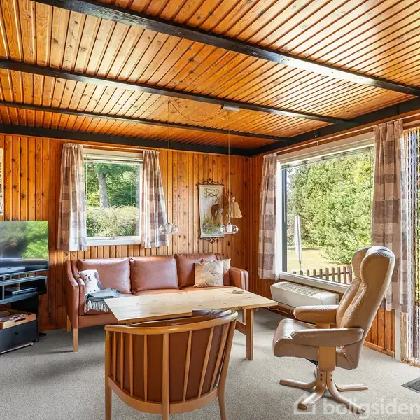 Stuen har træbeklædte vægge og loft, med et sofabord og stole placeret omkring. Store vinduer åbner ud mod en have. En fladskærms-tv står til venstre.