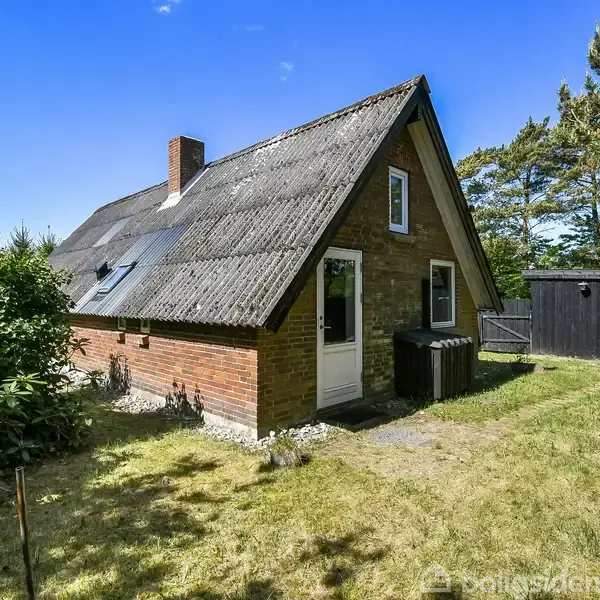 Et rødt murstenshus med skrånende tag står i en åben have med græs og omgivende træer. En hvid dør og to vinduer ses på siden.