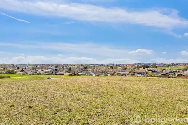 En åben mark strækker sig mod horisonten, hvor en udkant af en by er synlig under en klar blå himmel med få skyer.