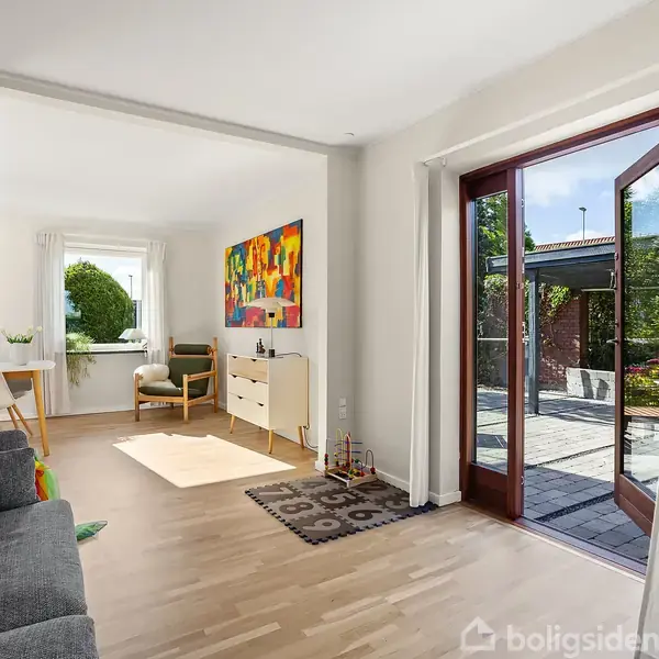 Stue med grå sofa, åbne franske døre til terrasse, farverigt maleri på væggen, kommode, stol ved vindue. Lyse trægulve og indbydende naturligt lys.