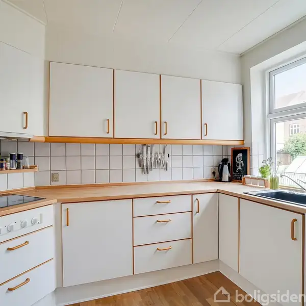 Et lyst køkken med hvide skabe og trækanter. Køkkenredskaber hænger på væggen, og vinduet viser udsigt over en grøn gård. Ingen tekst er synlig.