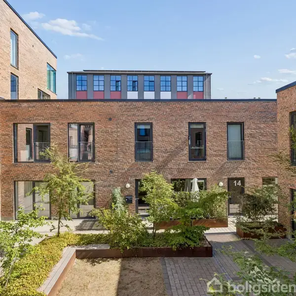 En moderne boligbygning med murstensfacade omkranser en lille, grøn gårdhave med plantekasser. Bygningerne har flere vinduer og døre, nogle med numrene 14 og 16. Klimaet er klart og solrigt.