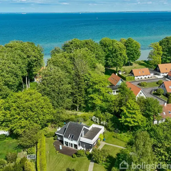 Hus i klassisk stil står i en velplejet have med en snoet stensti, frodige træer og farverige blomster. En lille pavillon er placeret til venstre i forgrunden.
