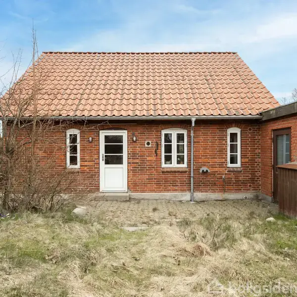 Et rødt murstenshus med tre vinduer og en hvid dør. Huset står i en græsset have med buske omkring. Taget er dækket med røde tegl.