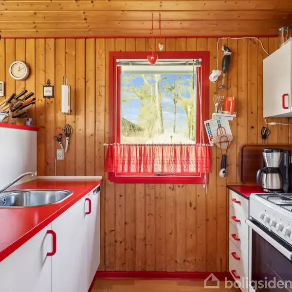 Et køkken med røde og hvide skabe, og en stålvask. Der er en gaskomfur til højre. Trævægge omgiver et vindue med rødt gardin. Ingen tekst fundet.