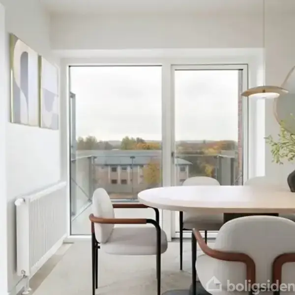Spisebord med fire stole står i spisestue ved store vinduer med udsigt til tage og træer. En dekorativ vase med grene samt abstrakte malerier pryder rummet.