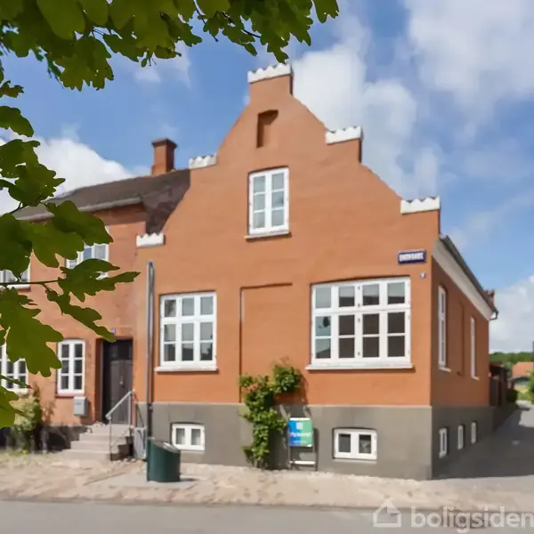 Rødt murstenshus med trapper. Husnummer 42B ses over indgangen. En grøn plante vokser op ad facaden. Taget er orangerødt. Blå himmel og skyer i baggrunden.