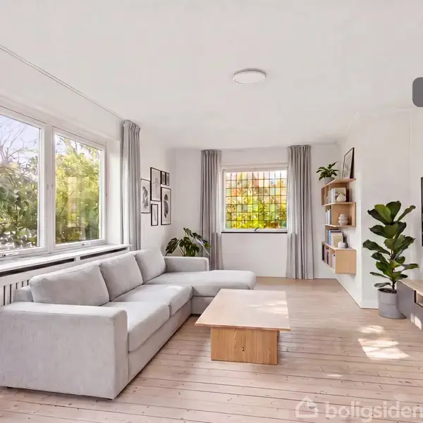 Grå sofa står i en stue med træbord foran, fladskærms-TV på væggen, store vinduer med gardiner, og grønne planter; værelse lyses op af naturligt lys. Tekst: "Visualisering".